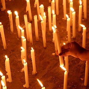 Lit candle being placed in the sand among other lit candles