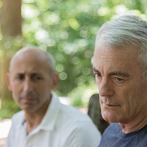 Close up of older man with serious expression with a man in background with concerned expression