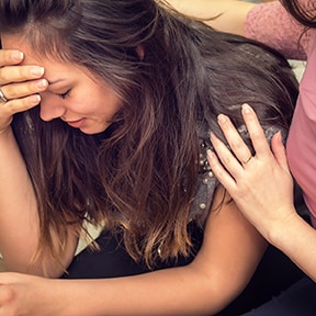 Close-up of an upset young woman being comforted by a friend