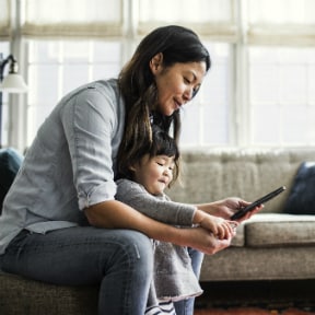Asian-American mother looking at a mobile device with her toddler daughter