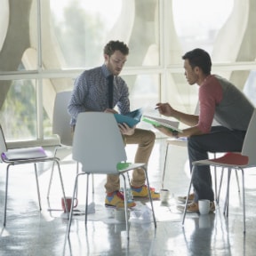 Two young business men, seated, talking over papers in their hands