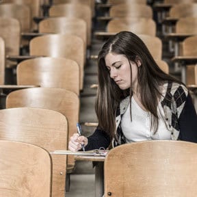 Young woman alone in a lecture hall seat, making notes