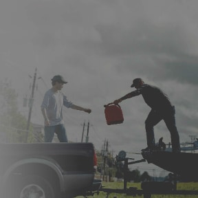 Man passing gasoline can from boat hitched to a pickup to another man on pickup bed