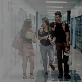 Boyfriend and girlfriend high school students walking in school hallway taking to another female student